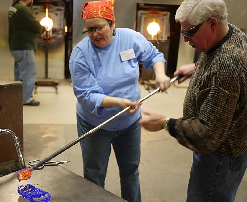 Grandpa is rolling his molten glass into bits of colored glass. Next he is going to mush it onto the vase…with the help of two master glass blowers.