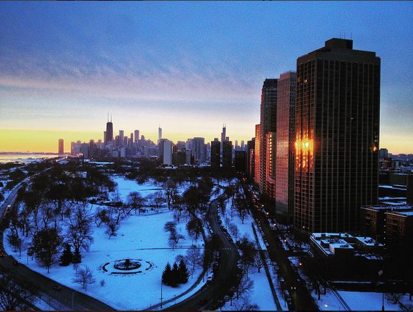 Chicago skyline at dusk in winter, viewed from a high vantage point with snow-covered Lincoln Park in the foreground and the city’s towers glowing in the last light.